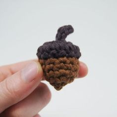 someone is holding a tiny crocheted acorn