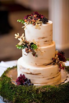 a three tiered white wedding cake with flowers and greenery on the top layer