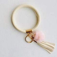 a white key chain with a pink tassel and gold plated metal ring on it