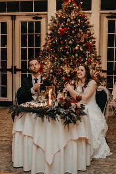 a man and woman sitting at a table in front of a christmas tree