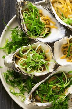 several oysters on a white plate topped with green sprouts and shredded cheese