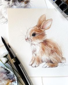 a watercolor painting of a rabbit sitting on top of a table next to paintbrushes