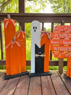 three wooden pumpkins decorated to look like ghostes and bats, on a porch