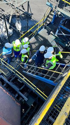 three men in safety vests standing on top of a large metal structure with yellow piping