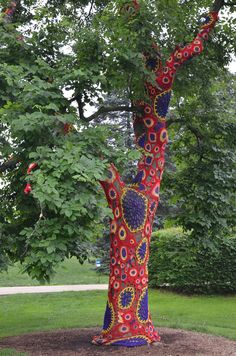 a red and blue sculpture in the shape of a woman's hand reaching up into a tree