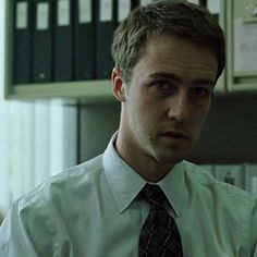 a man wearing a white shirt and tie in front of a computer desk with files on it