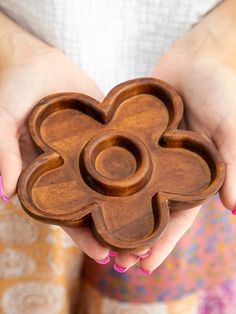 a woman holding a wooden flower shaped bowl in her hands with pink nail polish on her nails