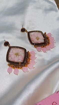 the earrings are adorned with pink flowers and gold beads on a white satin surface,