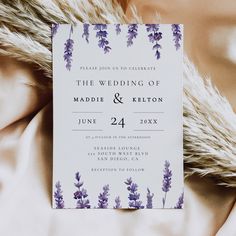 a wedding card with purple flowers on it sitting on top of a white bed sheet