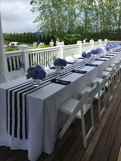 a long table is set up on the deck for an outdoor wedding reception with blue hydrangeas in vases