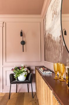 a room with pink walls and wooden flooring has a mirror on the wall next to a black chair