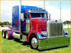 a red and blue semi truck parked on top of a lush green field