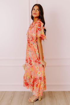 - Drape yourself in petals and twirl in the sun with this airy dress! - Chiffon material with a colorful abstract floral print - A built-in lining that ends above the ruffled hemline - A ruffled v-cut neckline with a tie detail - Short, loose ruffled sleeves - Pleated detail at the bodice - An elastic waistline - A flowy yet flattering silhouette that ends in a ruffled maxi length hemline Peach Ruffled Midi Dress For Garden Party, Coral Spring Vacation Dresses, Spring Coral Vacation Dresses, Spring Vacation Coral Dresses, Breezy Pink Ruffled Dress, Orange Floral Print Midi Dress For Vacation, Coral Dresses For Spring Vacation, Pink Breezy Dress With Ruffles, Breezy Pink Dress With Ruffles