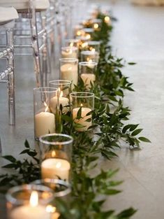 rows of candles are lined up on the floor with greenery in front of them