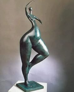 a bronze statue is standing on a white pedestal and has her arms in the air