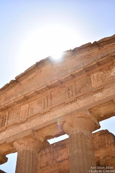 the sun shines brightly on an ancient building with columns and pillars in front of it