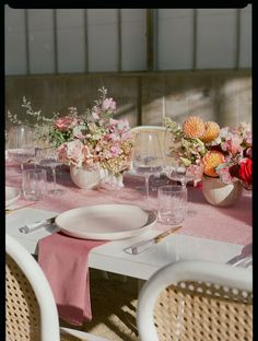 the table is set with pink and white plates, silverware, and flower centerpieces