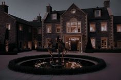 a large house lit up at night with lights on the front door and fountain in foreground