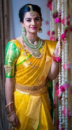 a woman in a yellow and green sari holding a beaded necklace on her neck