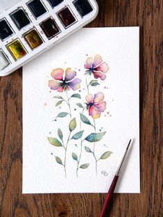 a watercolor painting of flowers on paper next to a paintbrush and some paints