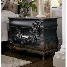 a black chest with flowers on it in front of a white bed and window sill