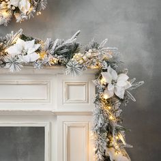 a fireplace decorated for christmas with white flowers and greenery