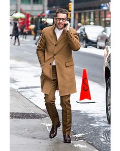 a man walking down the street talking on his cell phone while wearing a brown suit