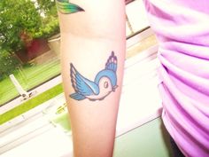 a small blue bird tattoo on the right forearm and arm, next to a woman's purple shirt