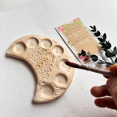 a hand holding a paintbrush next to a carved object