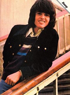 an old photo of a young man wearing a jacket and smiling at the camera while leaning on a railing