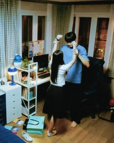 a man and woman standing in a living room next to a desk with a computer on it