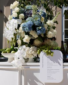 a bunch of flowers sitting on top of a white table next to bottles and glasses