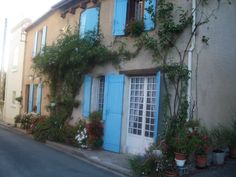 an old house with blue shutters and potted plants on the outside, next to a street