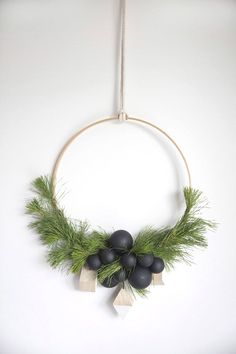 a wreath hanging on the wall with black balls and greenery attached to it's sides