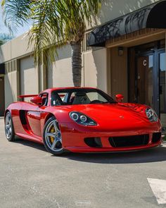 a red sports car parked in front of a palm tree on the side of a building