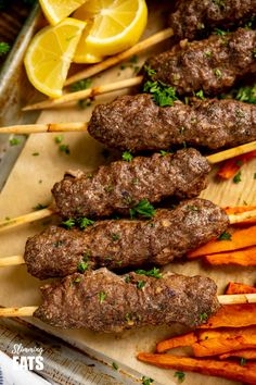 skewers of meat and carrots on a tray with lemon wedges next to them