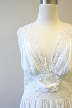 "Description: 1940s pale icy blue-gray night gown (it can look white or it can have a faint gray/blue cast to it). Silky rayon and lace, with a shimmery sheen. Deep V-neckline in the front and back with lace bodice. Gathered bust with a lace waist line. Gathered waist. Condition: In good condition. There is a small dark spot on the bodice, and a couple of tiny holes on the back of the gown. Designer: n/a Stated Size: n/a Measurements: Armpit to armpit: 18.5\" Bodice length: 15\" Overall length: White Vintage Night Gown, Vintage White Fitted Nightgown, White Lace V-neck Nightgown, White V-neck Nightgown With Delicate Lace, Vintage Lace V-neck Nightgown, Gown Designer, Women's Nightgowns, Icy Blue, Nightgowns