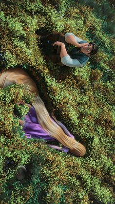 an aerial view of two people laying on the ground surrounded by green grass and bushes