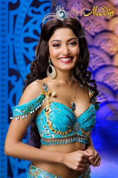 a woman in a blue and gold belly dance outfit smiling at the camera with her hands on her hips