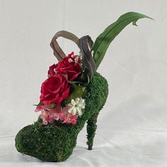 a shoe made out of grass with flowers on top and leaves sticking out of it