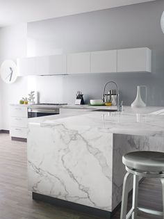 a kitchen with marble counter tops and stools in front of the island, along with white cabinets