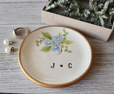 a white plate with blue flowers on it next to a box and two earrings in it