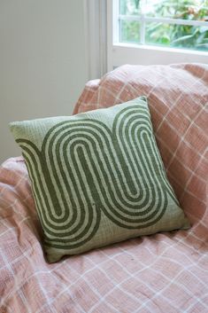 a green and white pillow sitting on top of a bed next to a pink comforter