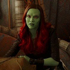 a woman with red hair and green makeup sitting on a couch in front of a mirror