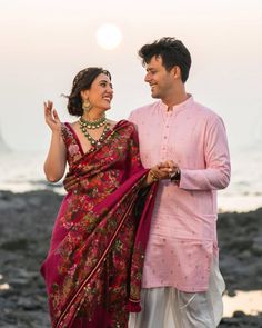 a man and woman standing next to each other near the ocean with their hands together