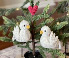 two crocheted white birds sitting on top of a tree in a pot with pine needles