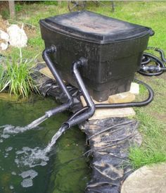 a large black trash can sitting on top of a rock next to a small pond