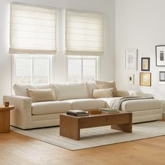 a living room with white couches and wooden coffee table in front of two windows