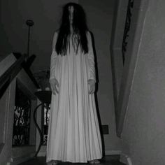 a woman with long hair wearing a white dress is standing on the stairs in a dark room