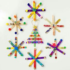 four popsicle christmas tree ornaments on a white surface with colorful beads and pins attached to them